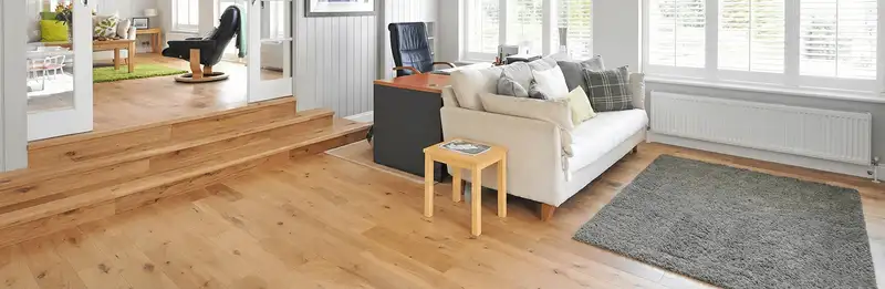 A modern living room with professionally installed laminate flooring, a beige sofa, a small side table, a gray rug, and large windows with white shutters in Richmond, VA